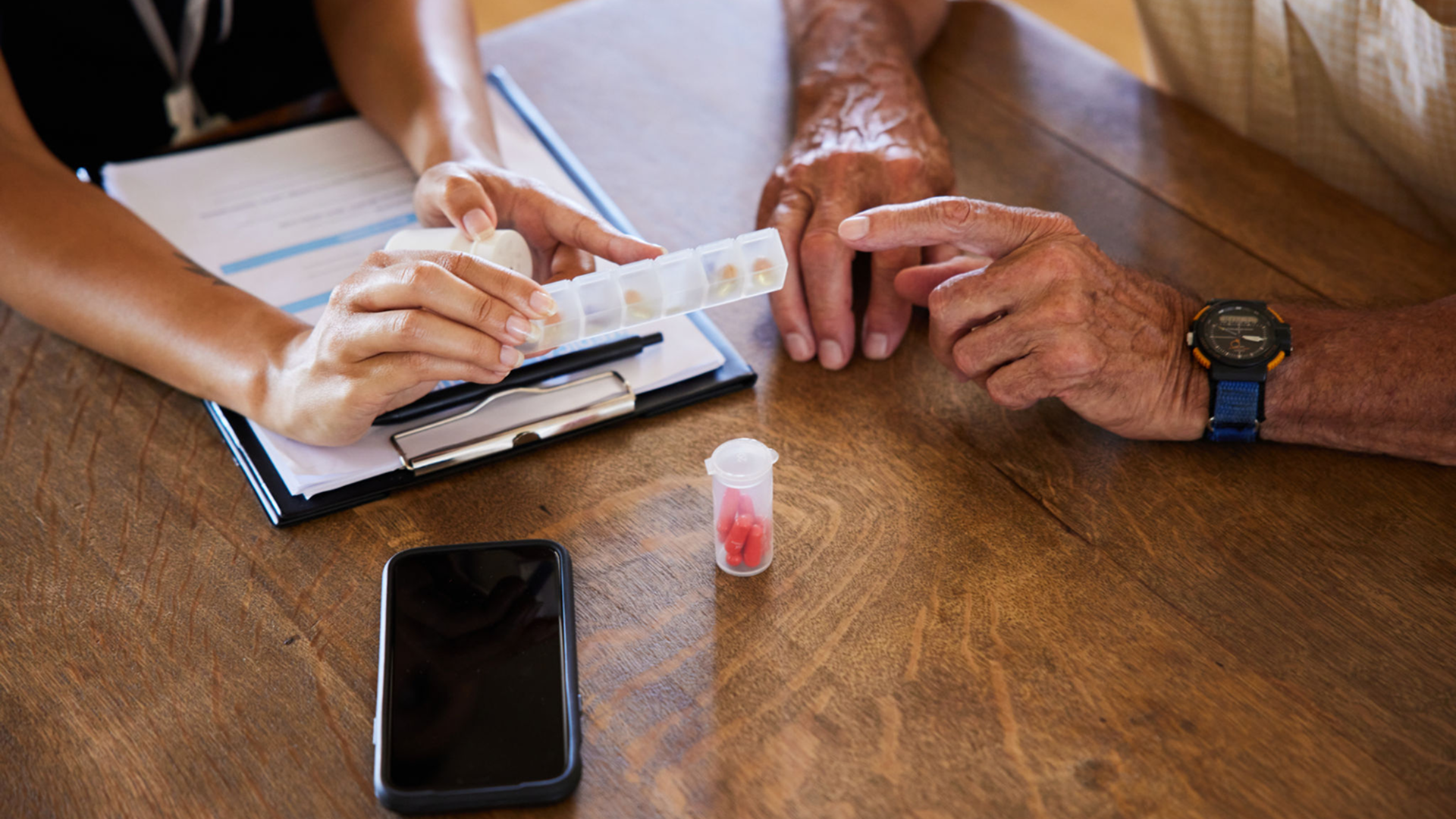 Hands organizing pills at a wooden table.